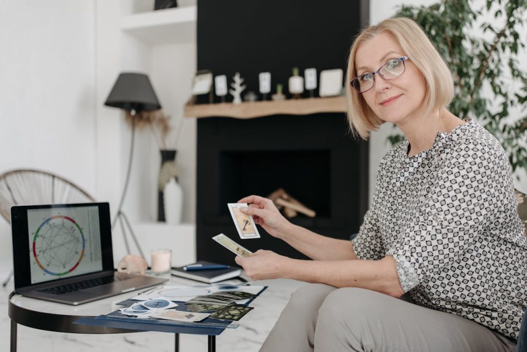 Woman with tarot cards using laptop for astrology reading in cozy living room.